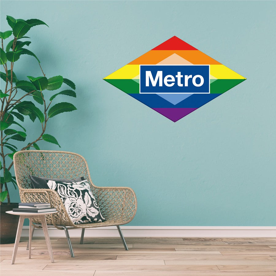 Logotipo Metro arcoíris en pared azul, interior moderno con silla y planta decorativa