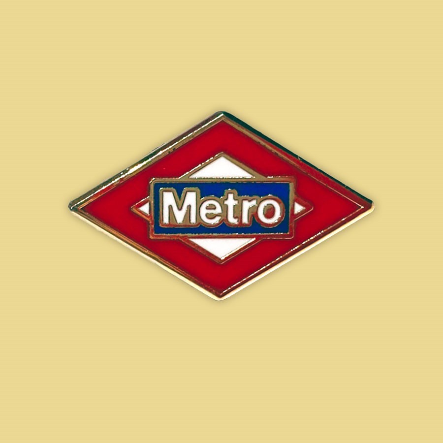 Insignia metálica Metro Madrid, fondo beige, diamante rojo y blanco, letras azules y blancas.
