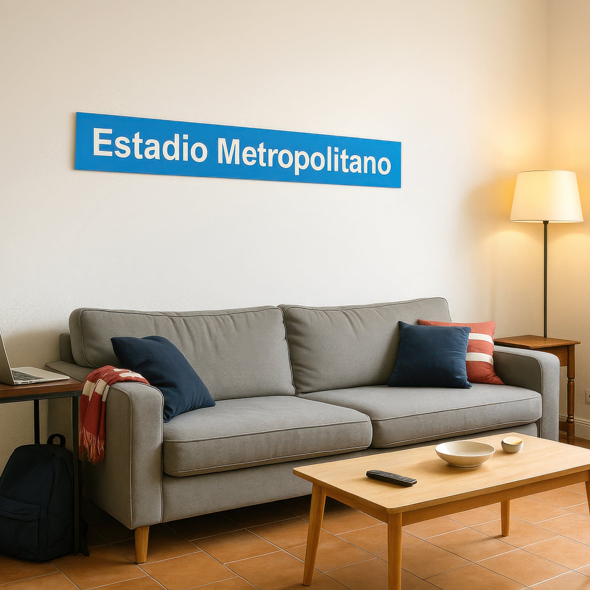 Salón de estudiante moderno con sofá gris, almohadas, lámpara de pie y letrero Estadio Metropolitano