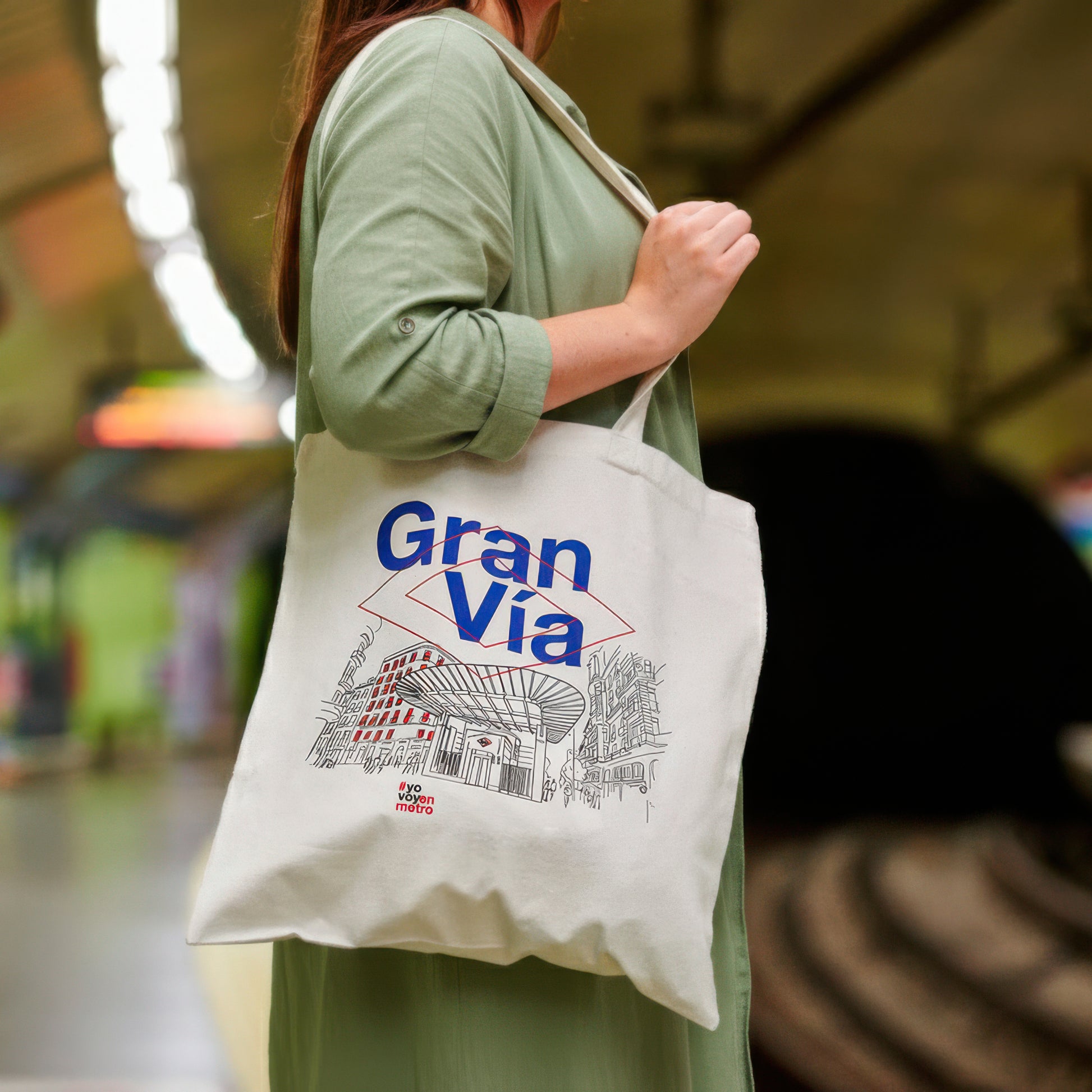 Mujer con bolso de tela blanca Gran Vía en metro, ilustración de edificio urbano.
