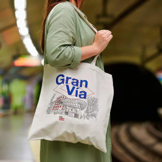 Mujer con bolso de tela blanca Gran Vía en metro, ilustración de edificio urbano.