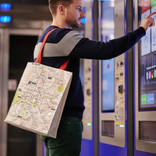 Hombre con bolsa ecológica estampada con mapa del metro, usando máquina expendedora en estación.