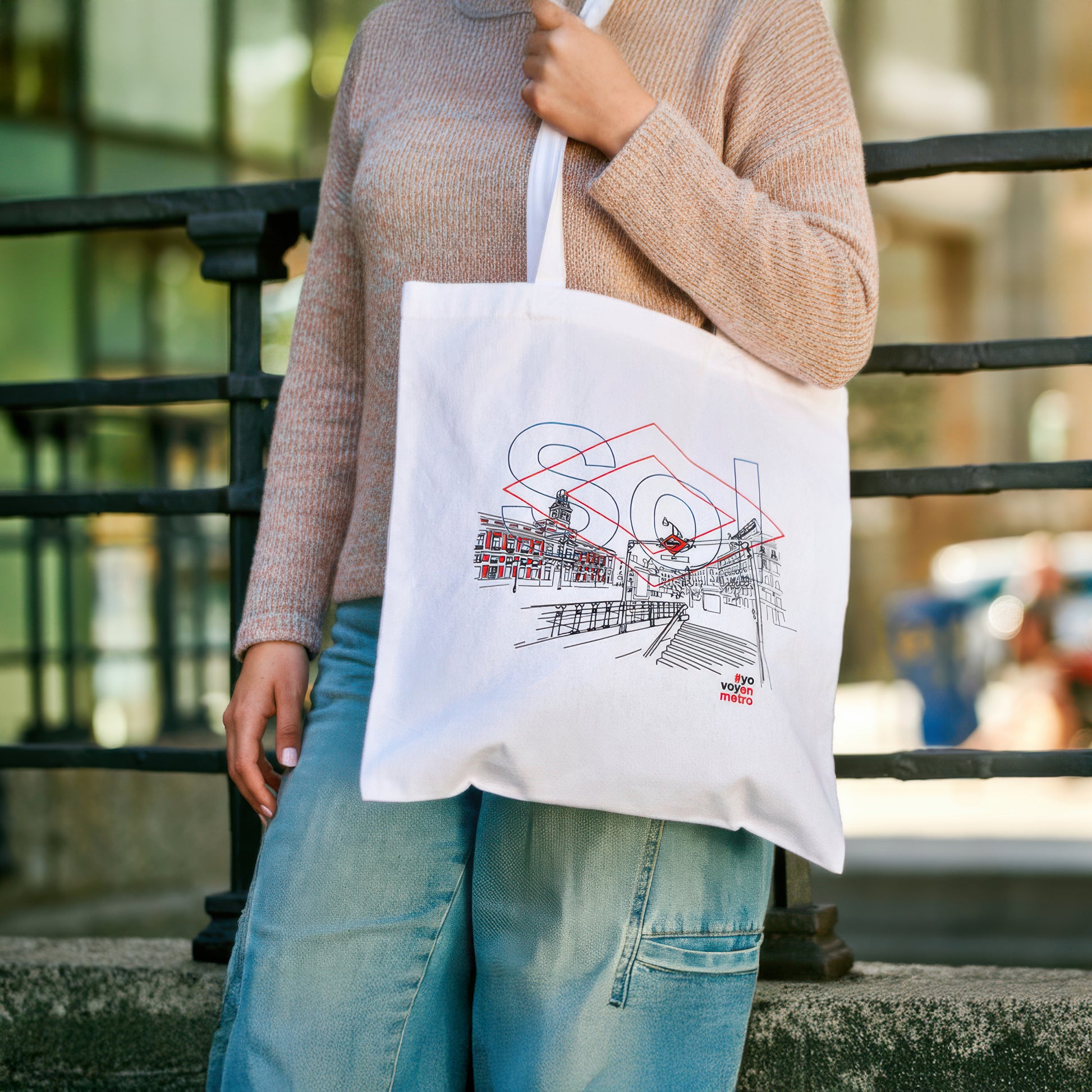 Mujer con bolso de tela blanco ilustrado con Puerta del Sol de Madrid en exterior urbano.