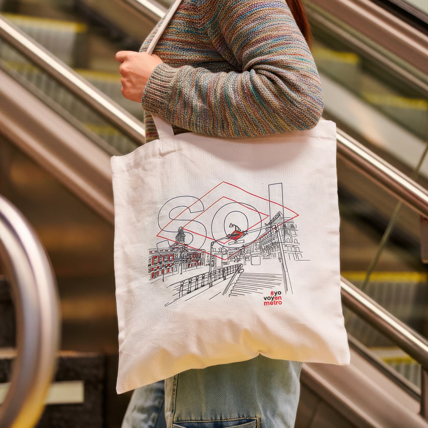 Bolsa de tela con ilustración de la Puerta del Sol y texto #yovoyenmetro, escalera mecánica