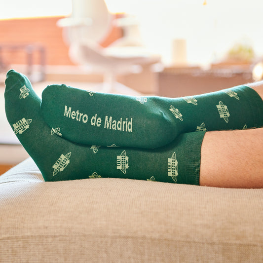 Calcetines verdes Metro de Madrid con diseño de estación, puestos en un sofá en casa