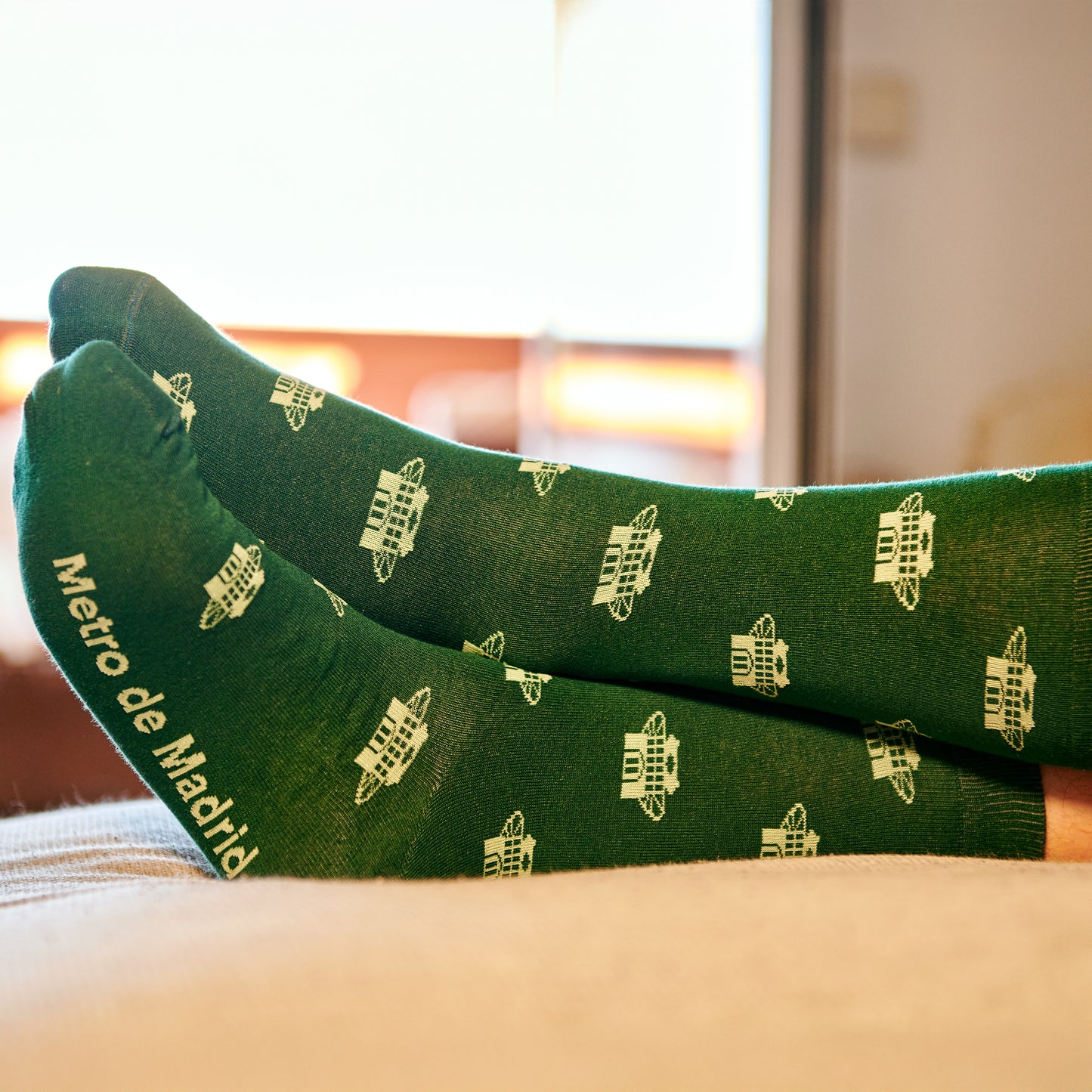 Calcetines verdes Metro de Madrid con dibujos blancos, persona descansando en sofá