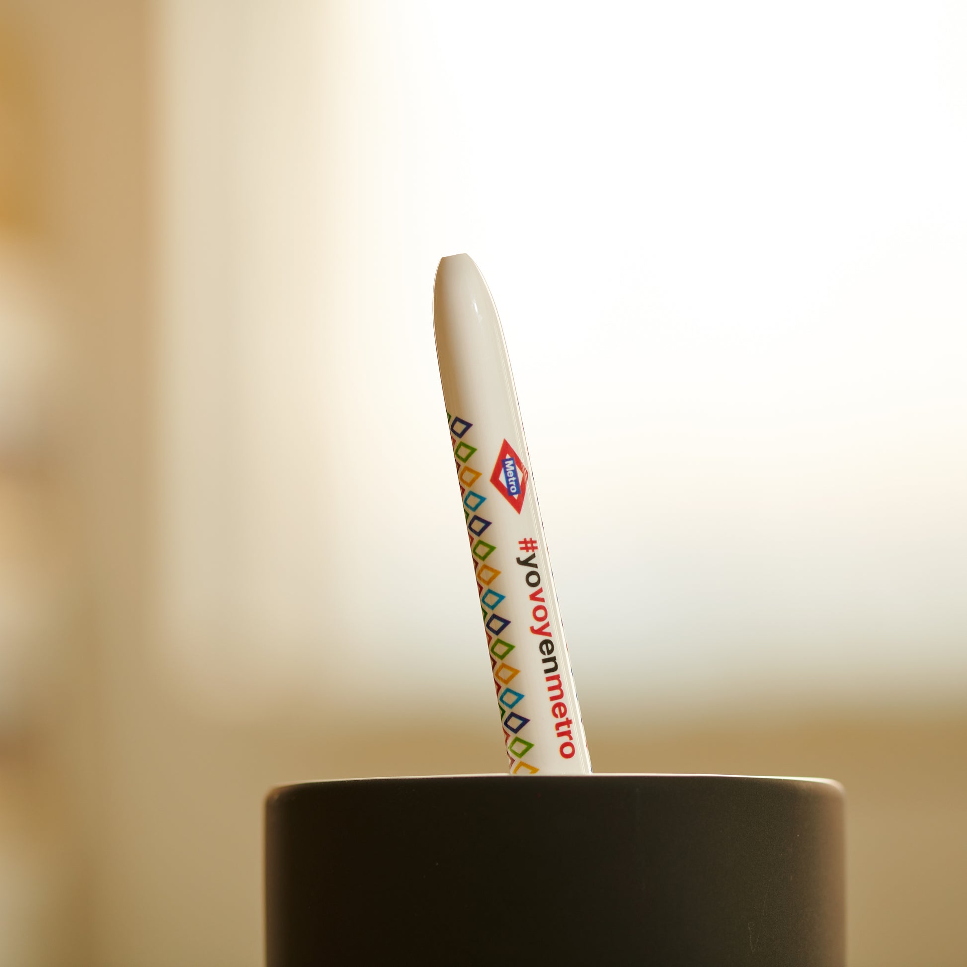 Bolígrafo blanco metro CDMX con hashtag #yovoyenmetro en vaso negro, fondo desenfocado.