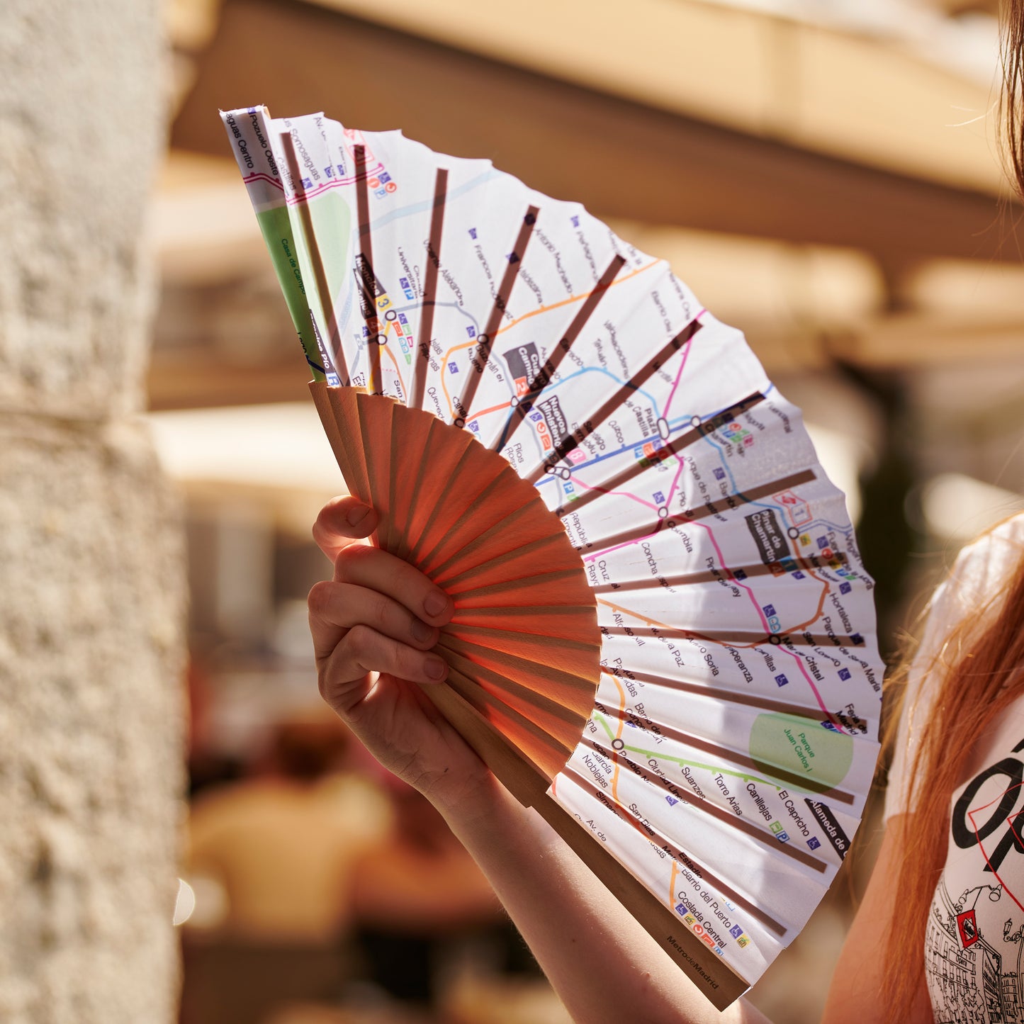 Abanico de papel con diseño de mapa de metro, sujetado por una mano en un entorno urbano