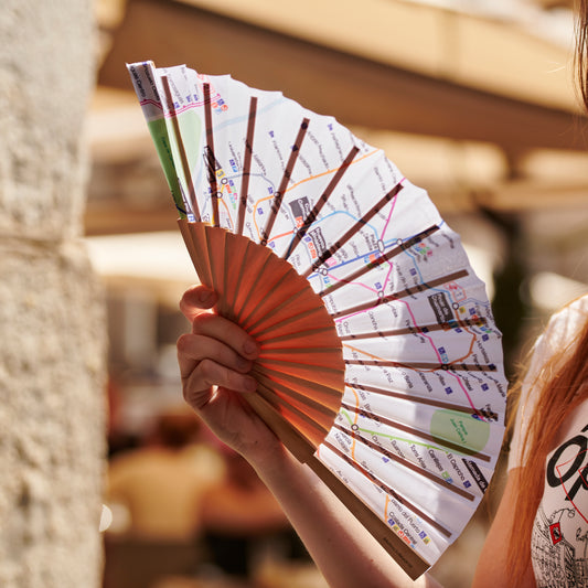 Abanico de papel con diseño de mapa de metro, sujetado por una mano en un entorno urbano