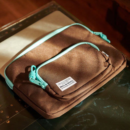 Funda marrón para laptop con cremalleras turquesa y etiqueta Metro de Madrid sobre mesa