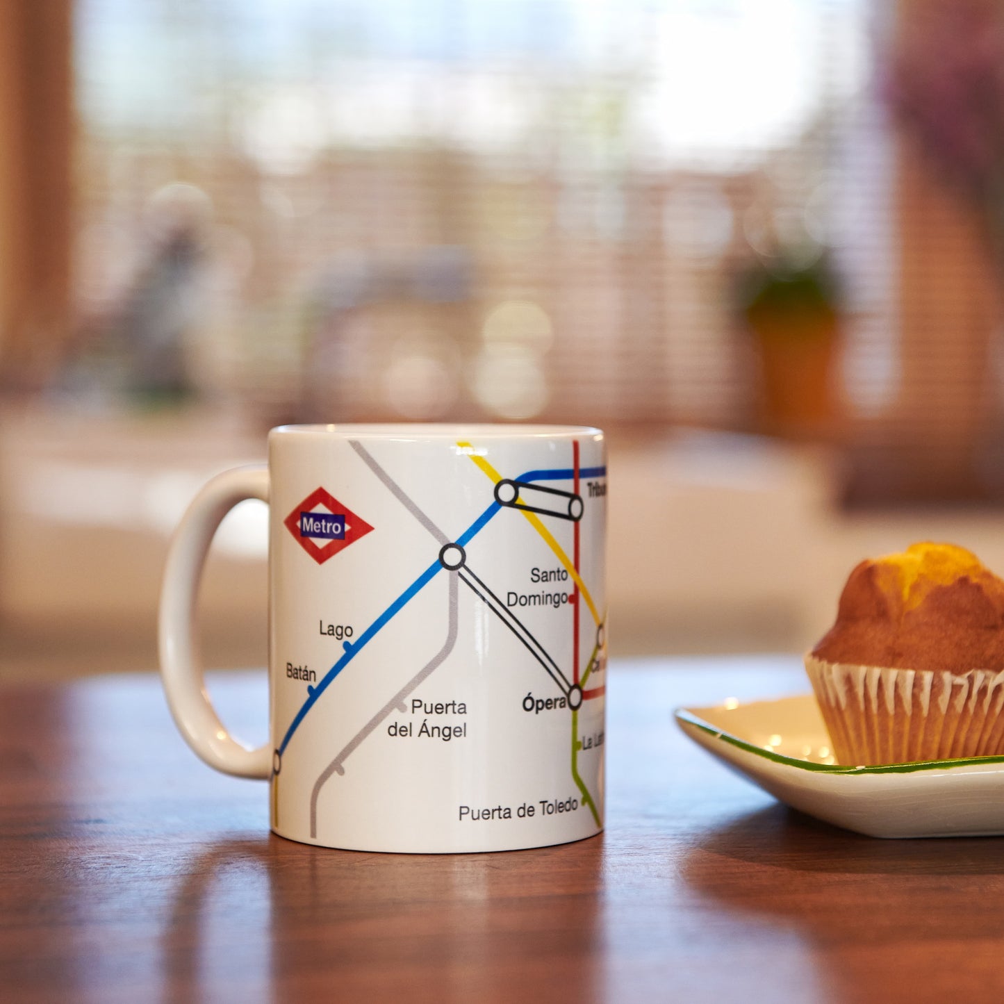 Taza con diseño del metro de Madrid y magdalena en plato sobre mesa de madera