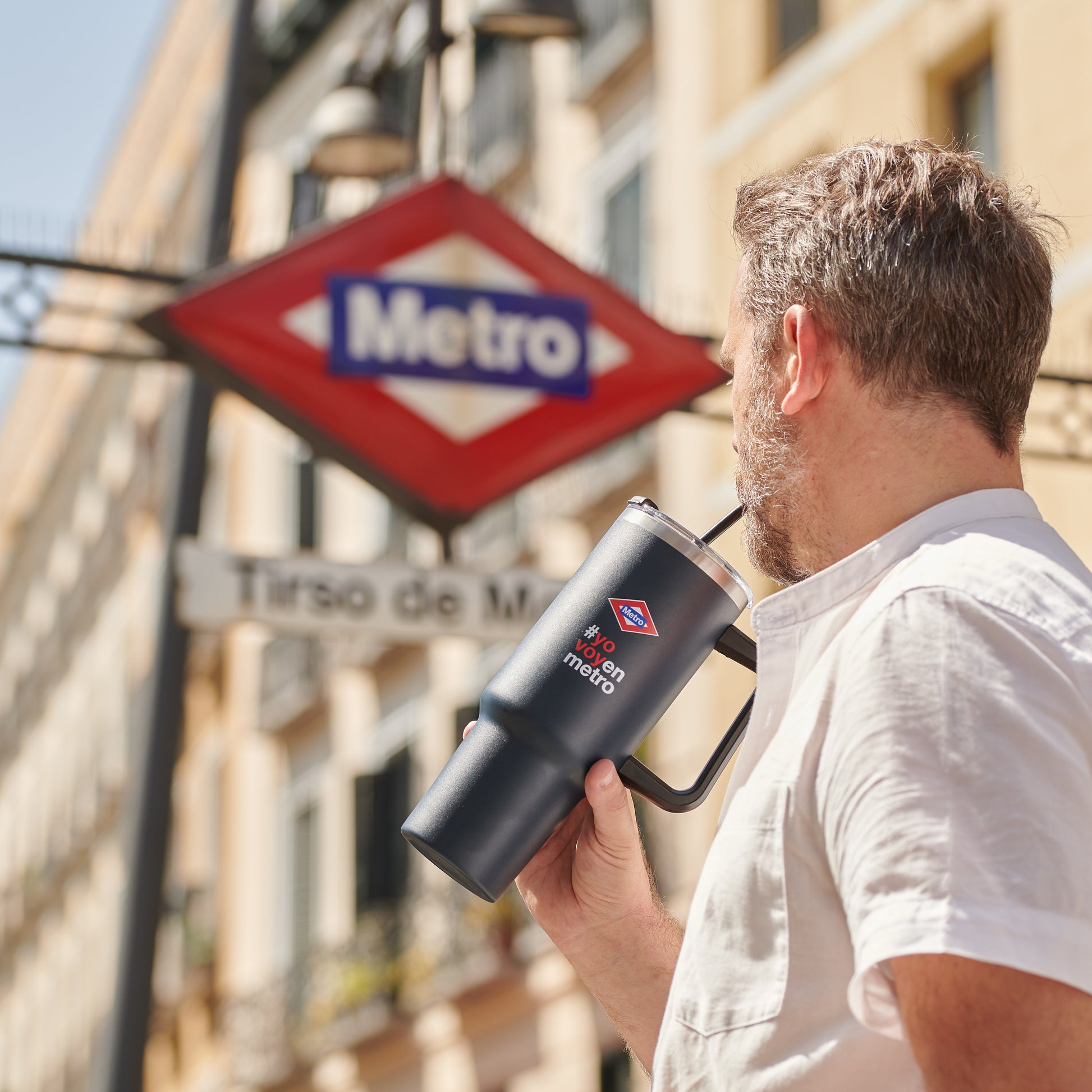 Hombre con termo negro de Metro de Madrid frente a señal de estación Tirso de Molina