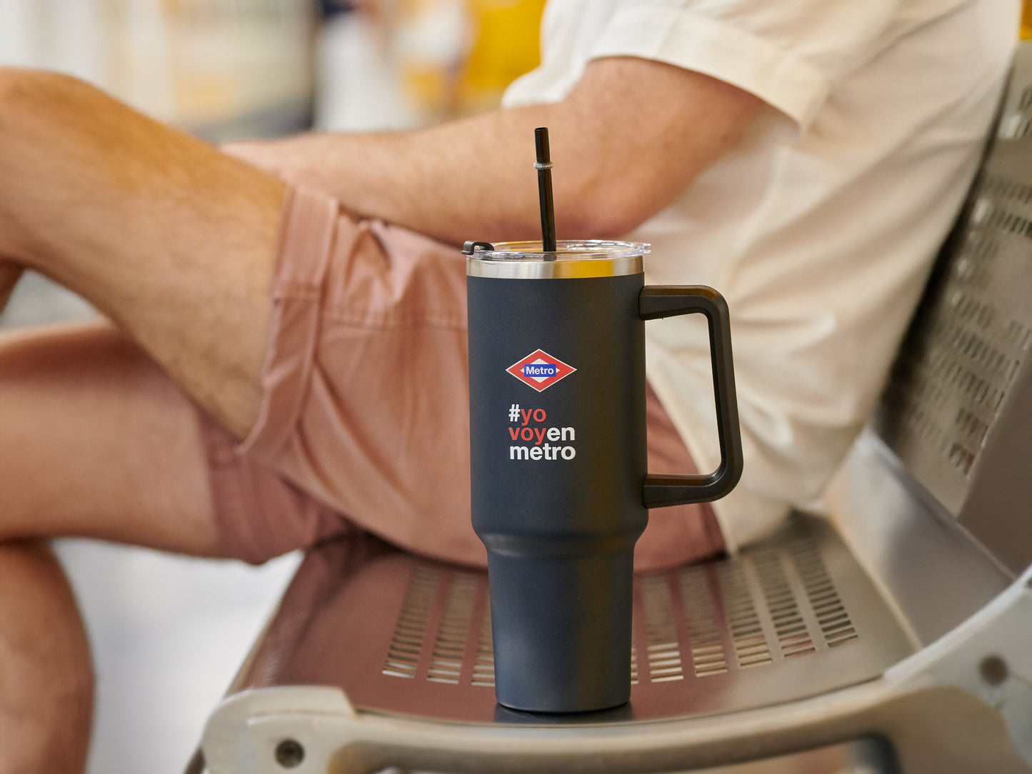 Vaso térmico negro Metro CDMX con popote en banca, persona con shorts rosa sentado