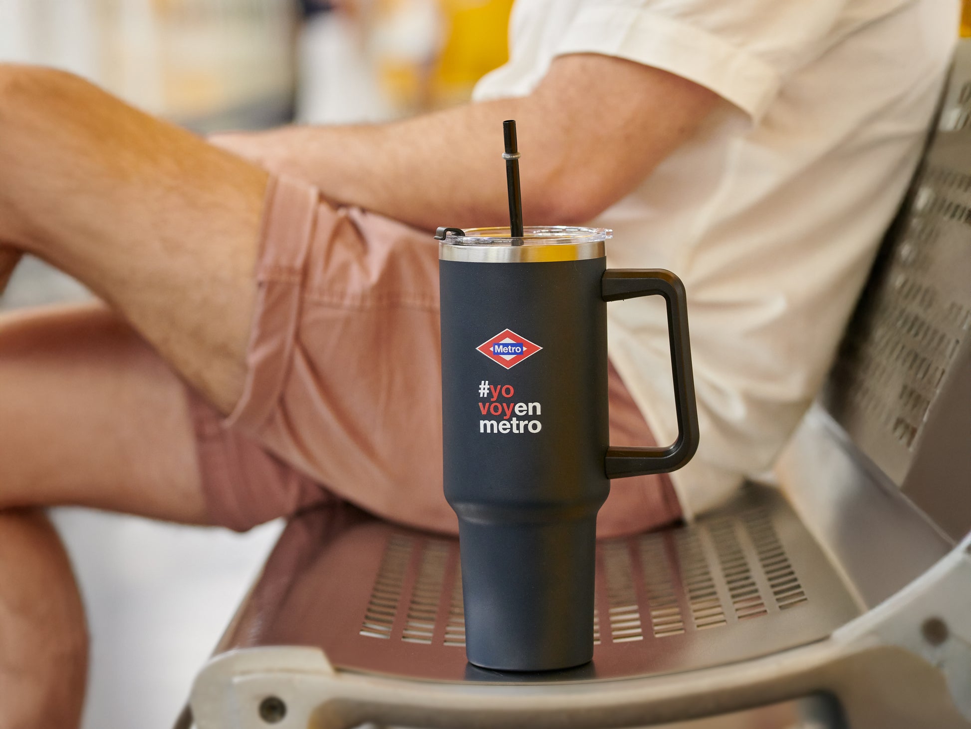 Vaso térmico negro Metro CDMX con popote en banca, persona con shorts rosa sentado