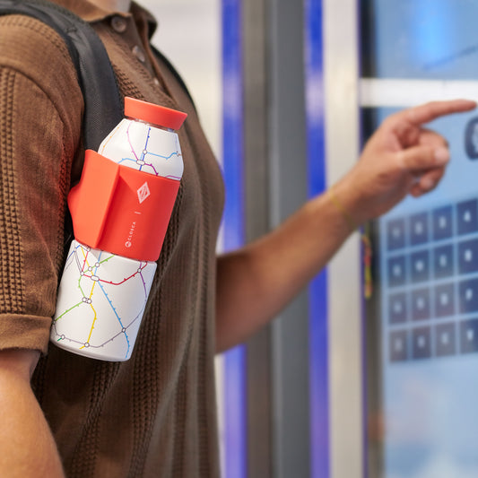 Persona con botella blanca de mapa de metro y funda roja, usando pantalla táctil en estación.