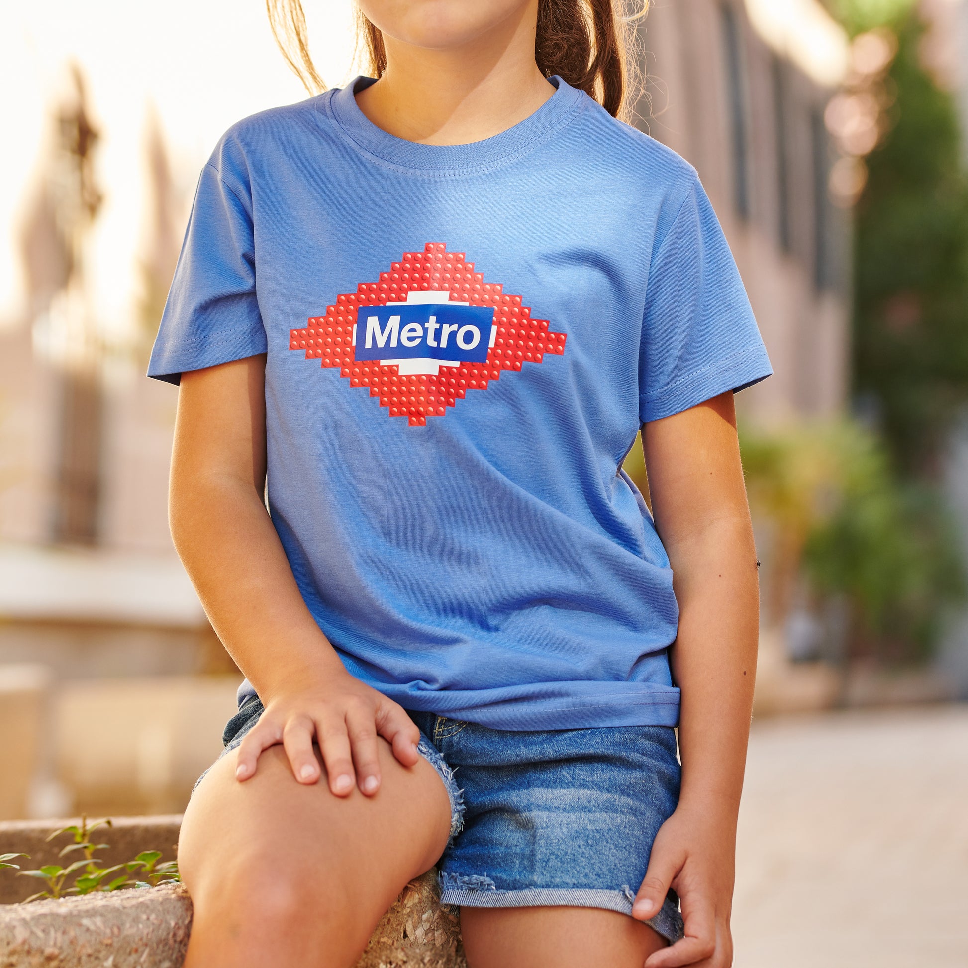 Niña con camiseta azul Metro Madrid y pantalón corto vaquero en calle urbana