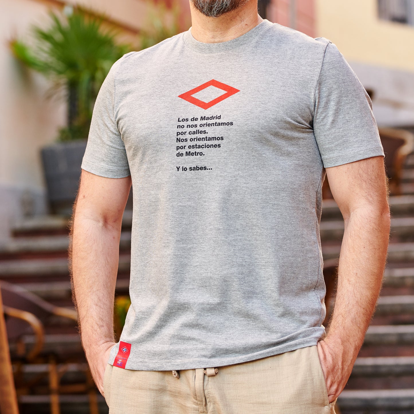Hombre con camiseta gris de mensaje sobre el Metro de Madrid, fondo urbano con escaleras y plantas