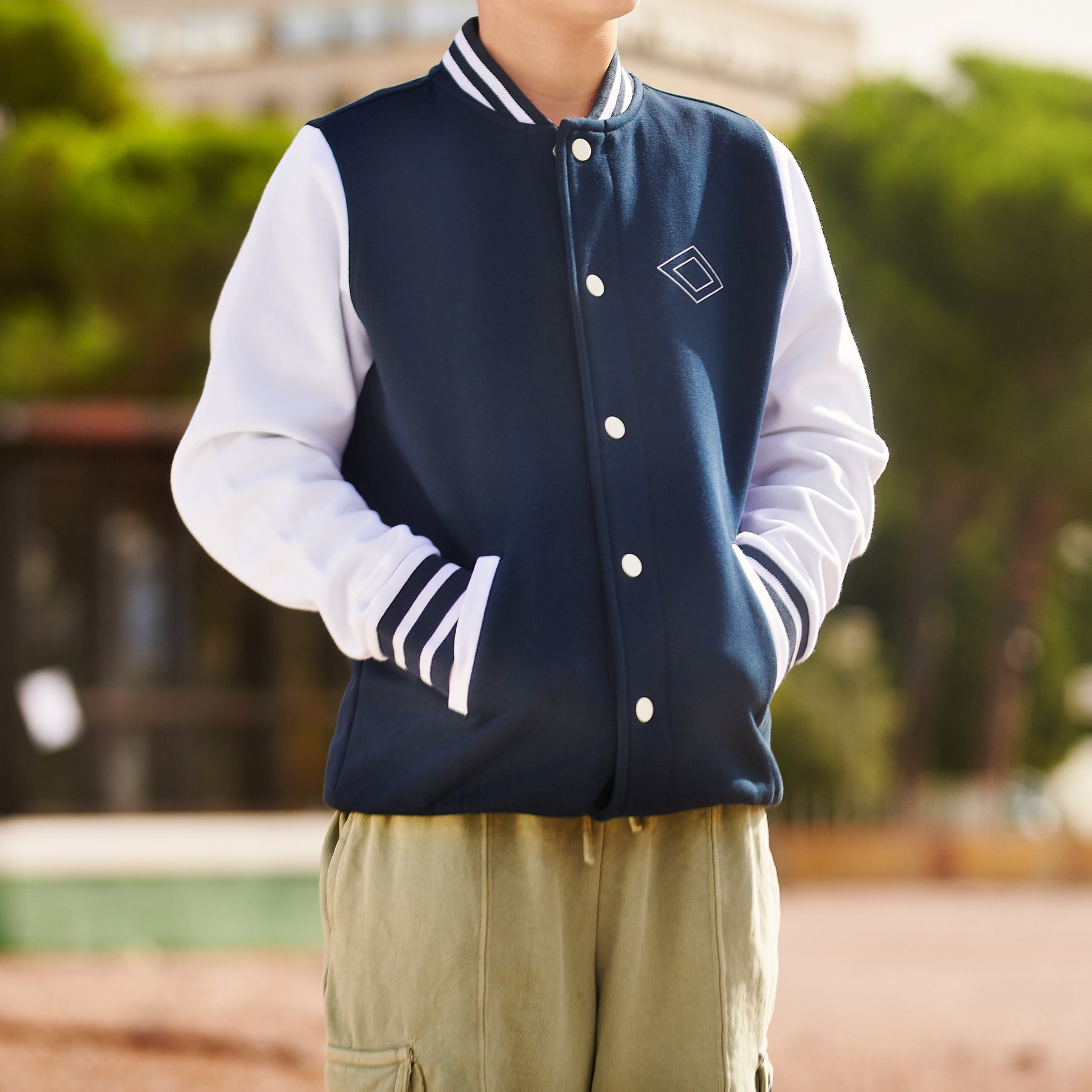 Chico con chaqueta varsity azul marino y blanca, al aire libre, moda juvenil urbana