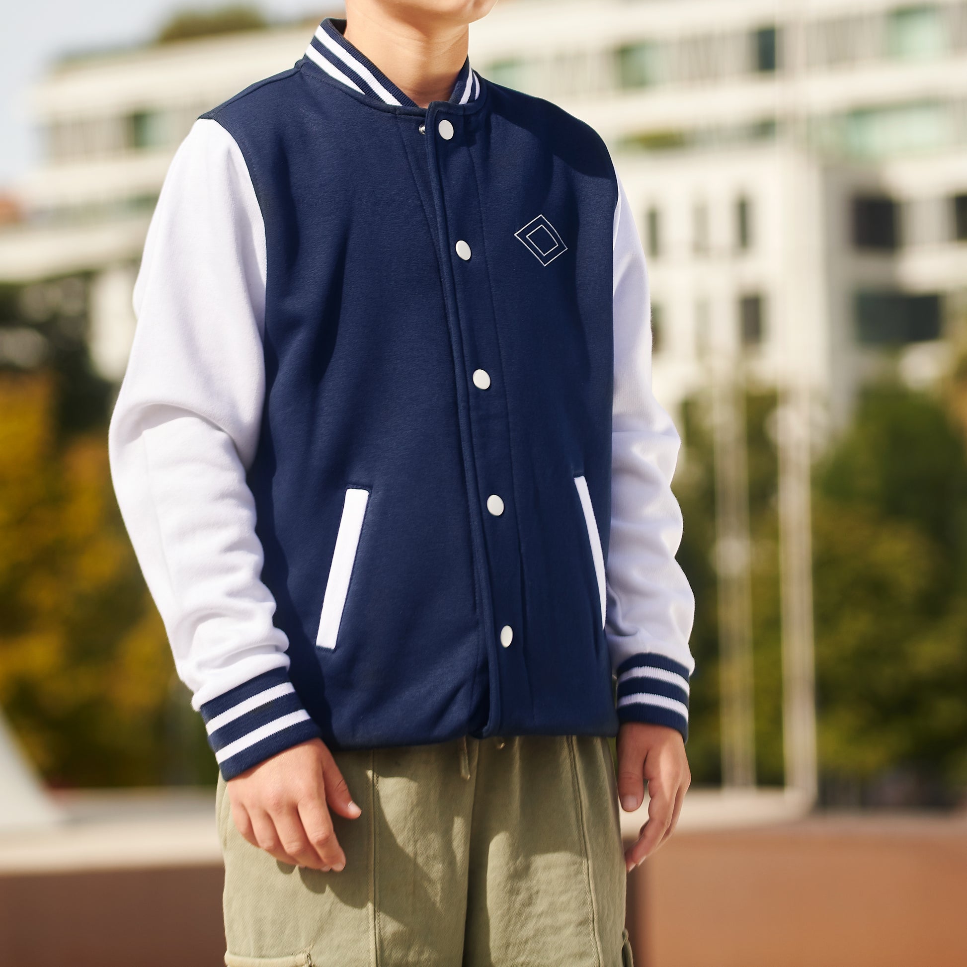 Chico con chaqueta varsity azul marino y blanco, fondo urbano, moda juvenil.