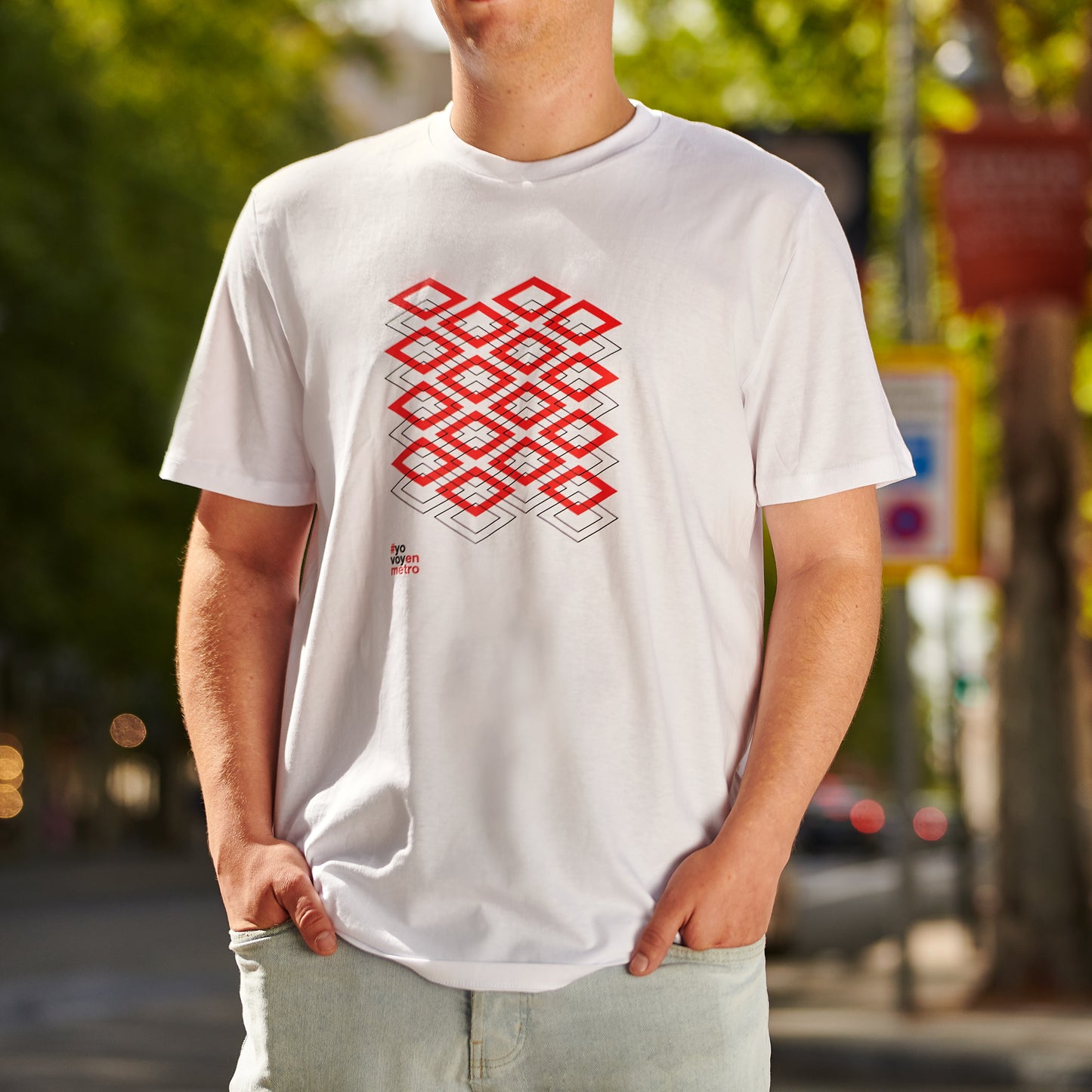 Hombre con camiseta blanca con diseño geométrico rojo y negro, en calle arbolada