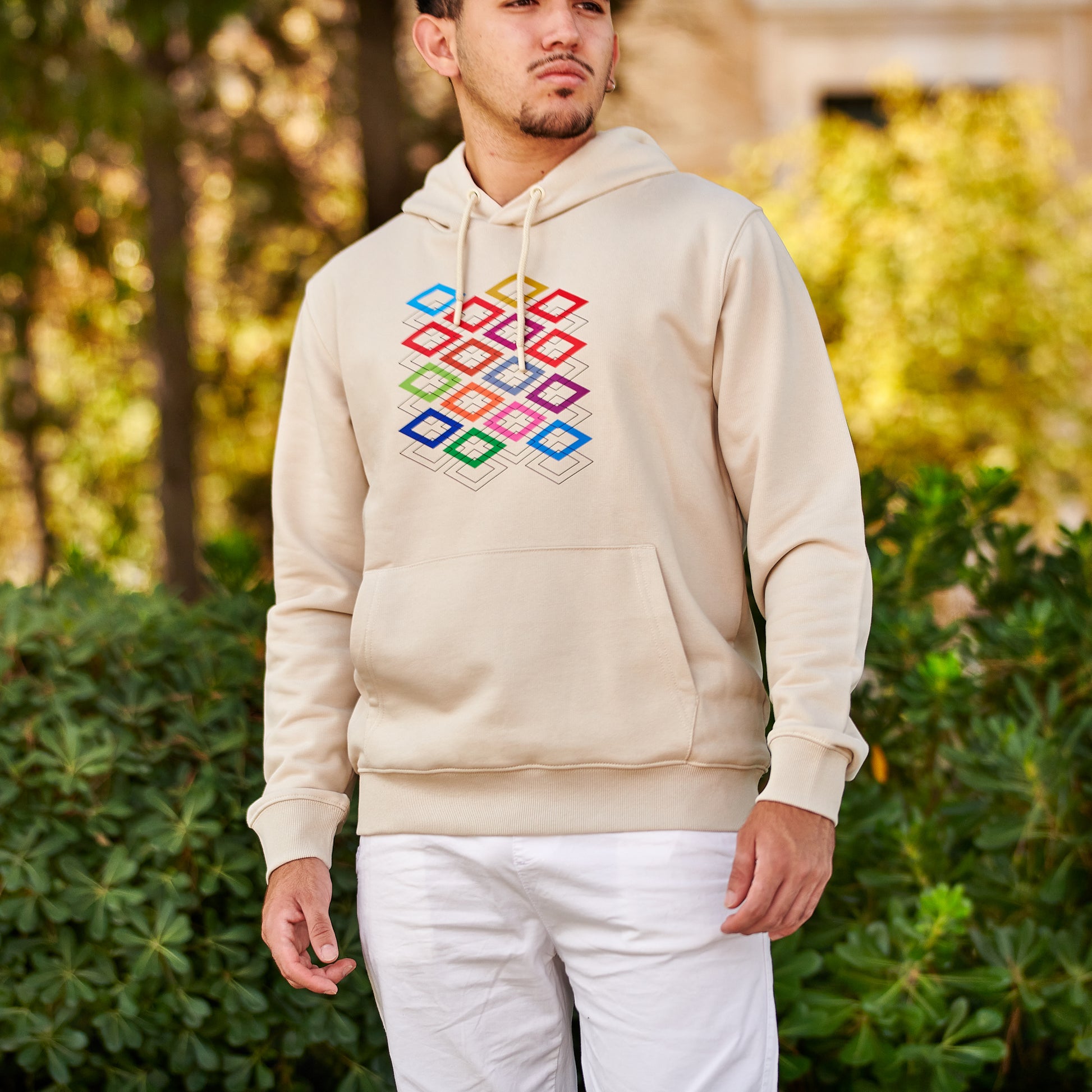 Hombre con sudadera beige de capucha y estampado geométrico colorido al aire libre