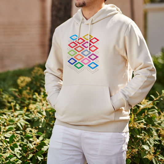 Hombre con sudadera beige de capucha y diseño geométrico colorido, exterior soleado.