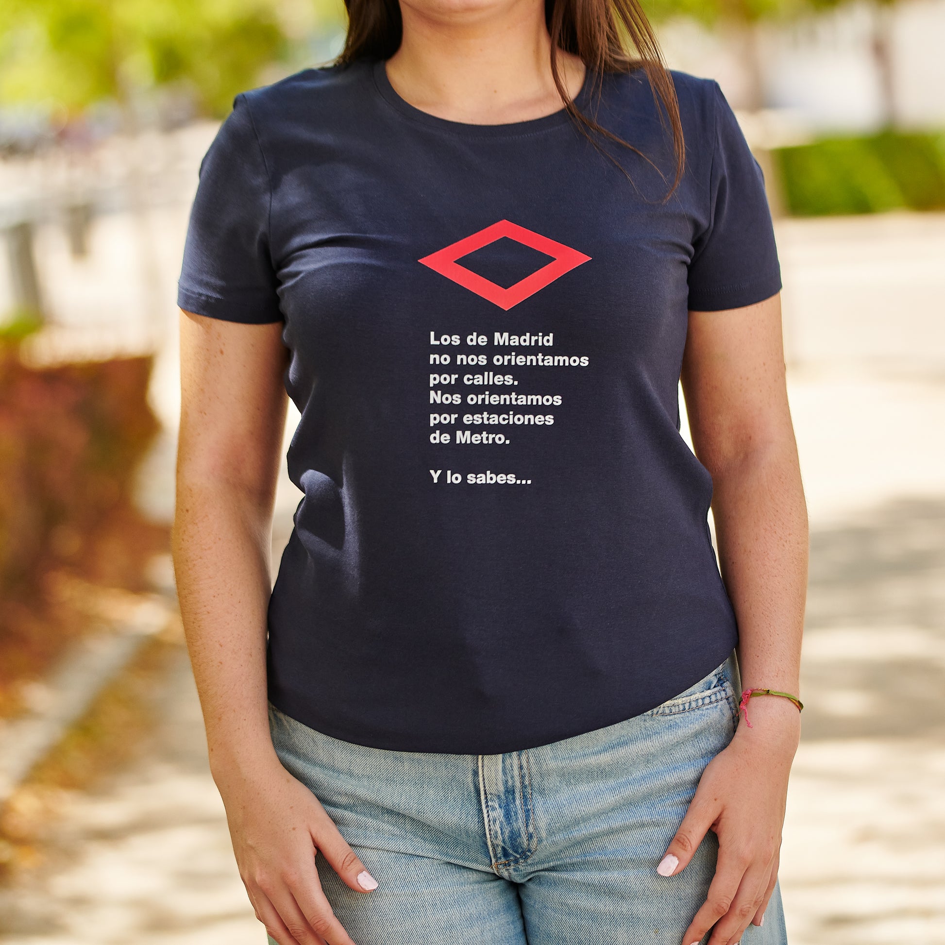 Mujer con camiseta azul marino con texto sobre Madrid y símbolo del Metro, en exterior urbano.
