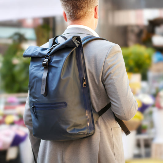 Hombre con mochila impermeable azul oscuro en traje gris en entorno urbano