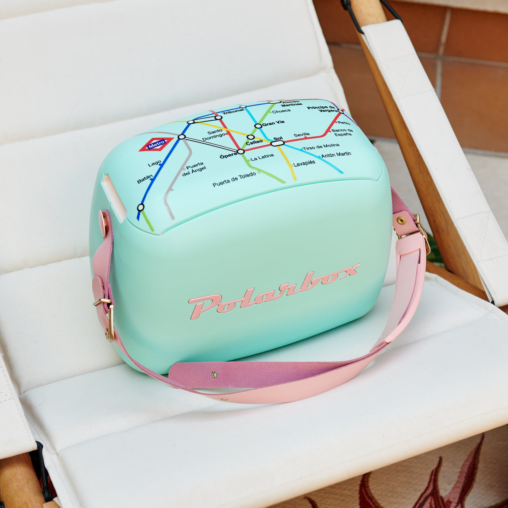 Nevera portátil Polarbox menta con correa rosa y diseño de mapa de metro, sobre silla blanca