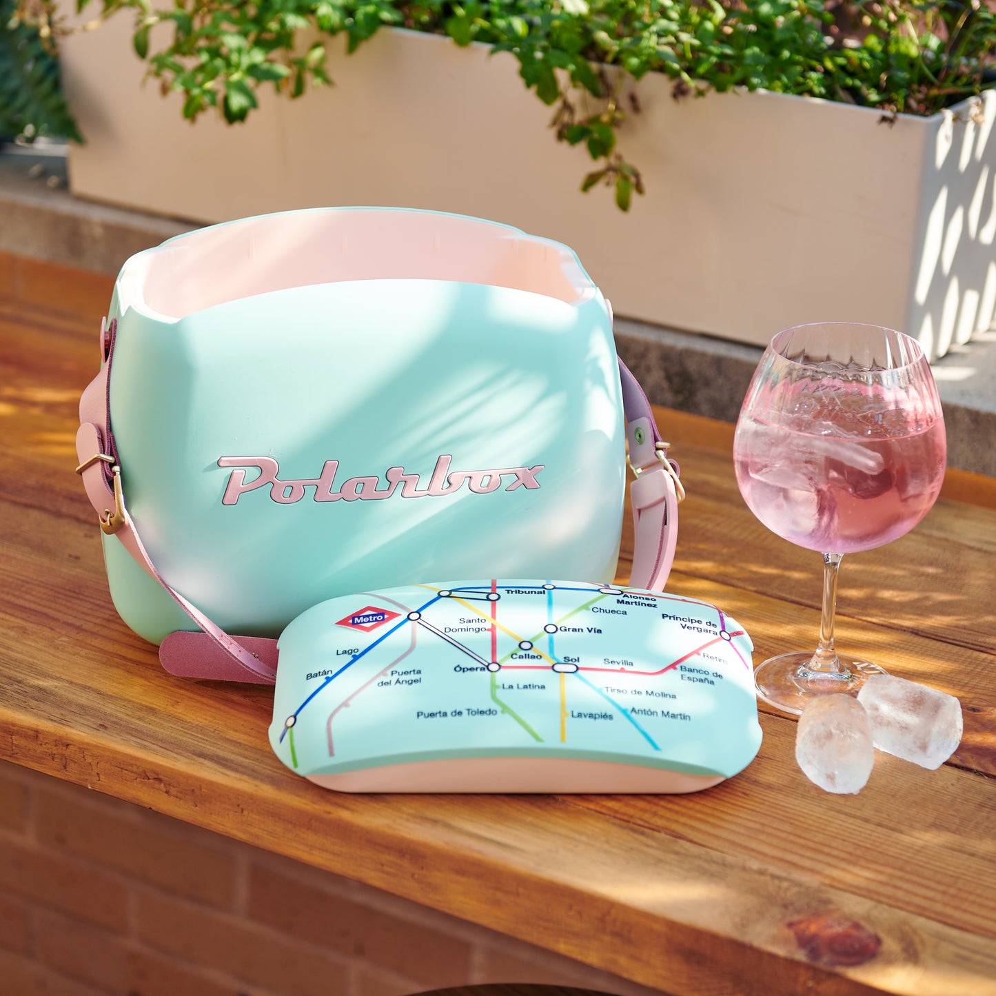 Nevera Polarbox azul pastel sobre mesa de madera con copa de bebida rosada y bloques de hielo