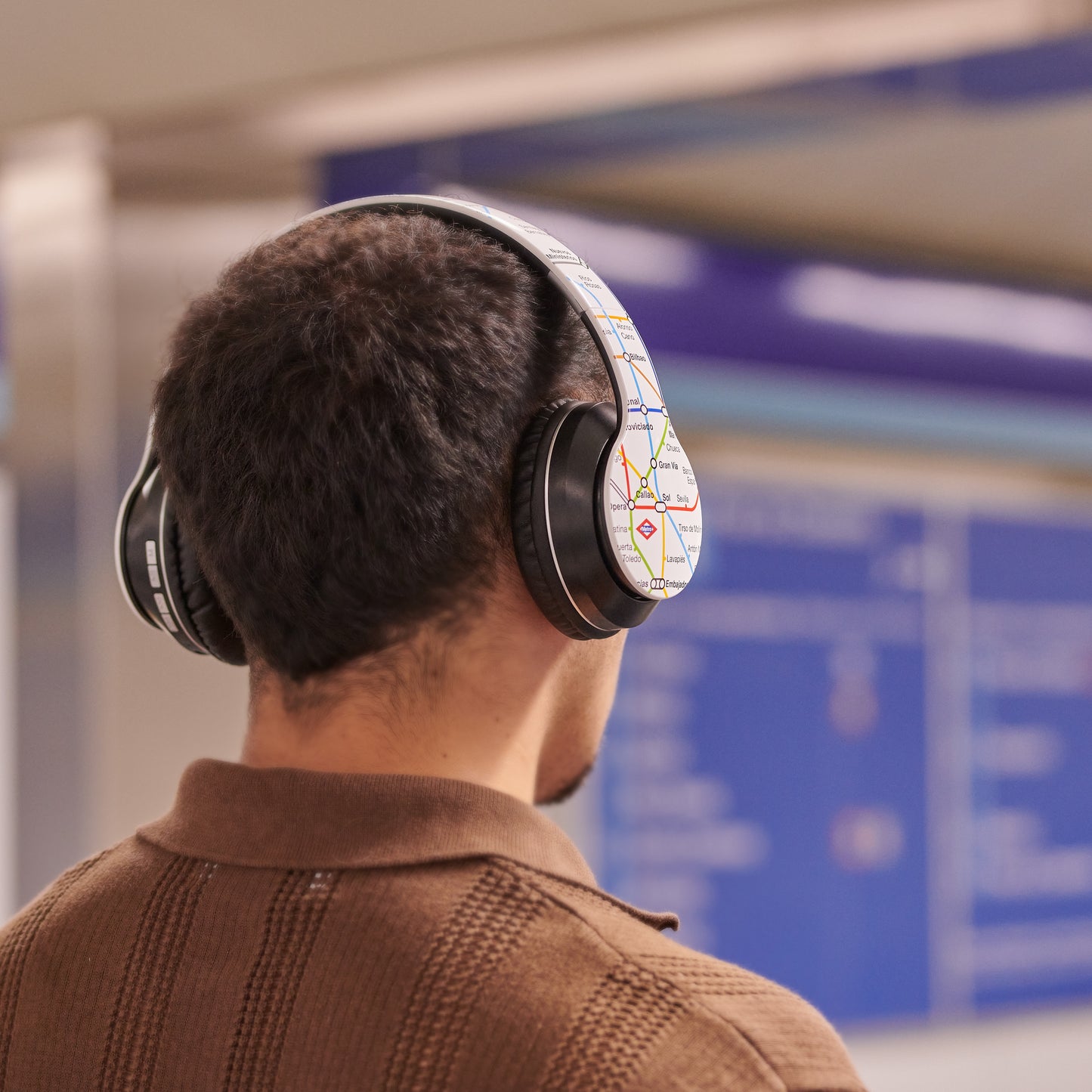 Hombre con auriculares decorados con mapa de metro en estación de transporte público