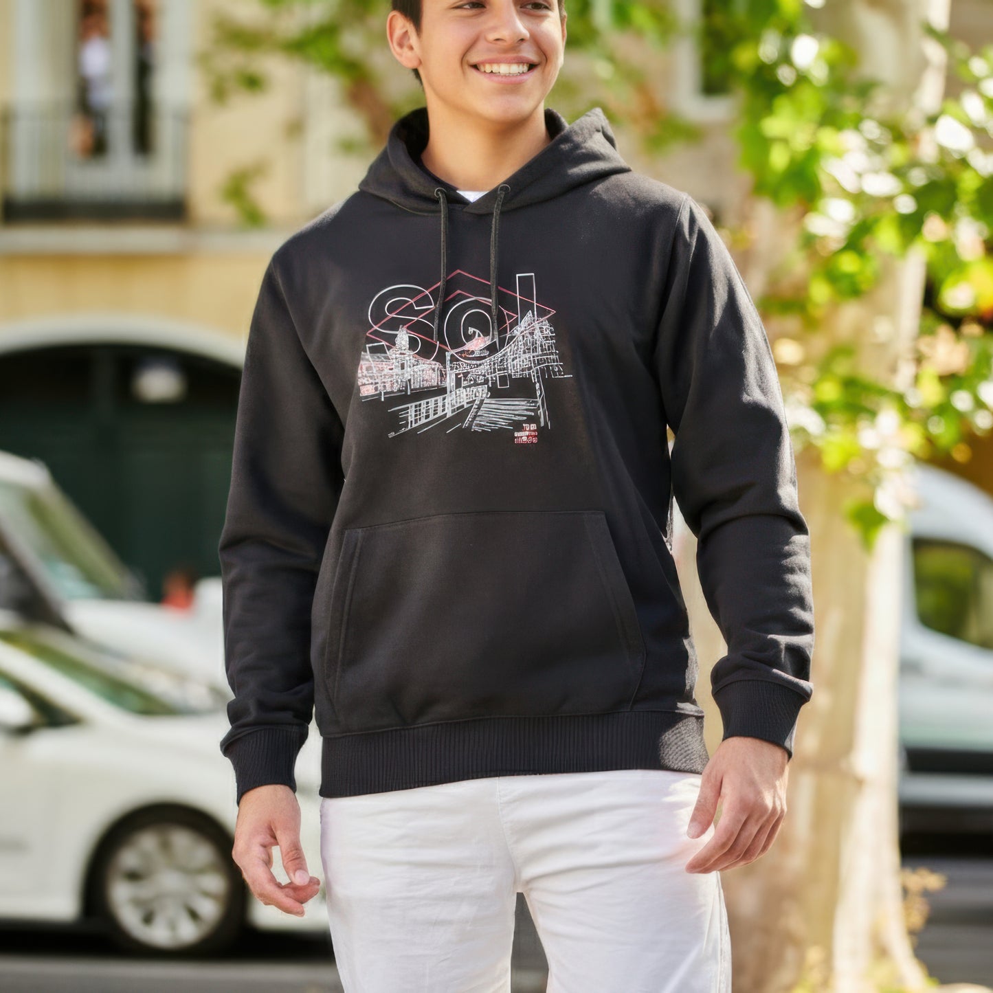 Chico con sudadera negra de capucha Sol y pantalón blanco en calle urbana soleada