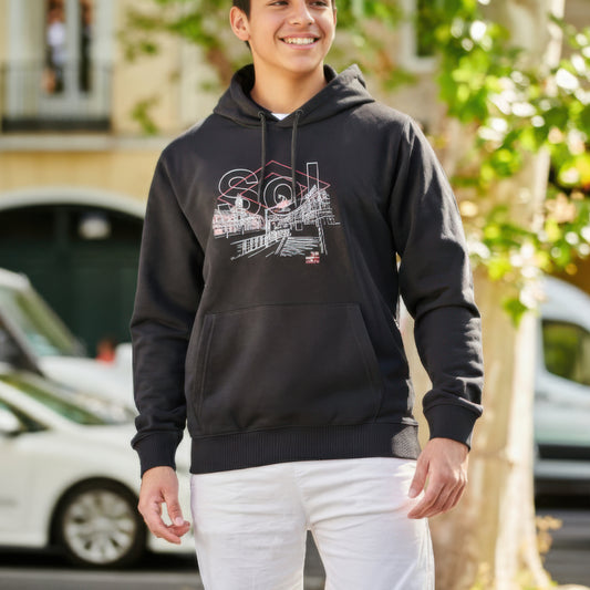 Chico con sudadera negra de capucha Sol y pantalón blanco en calle urbana soleada