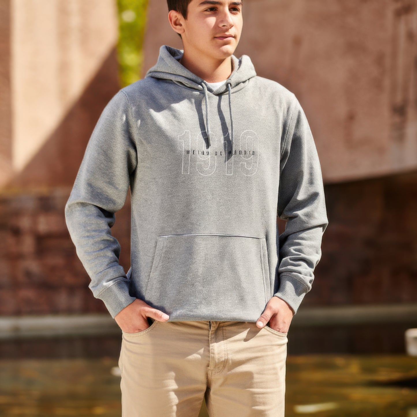 Joven con sudadera gris 1919 y pantalón beige de pie al aire libre