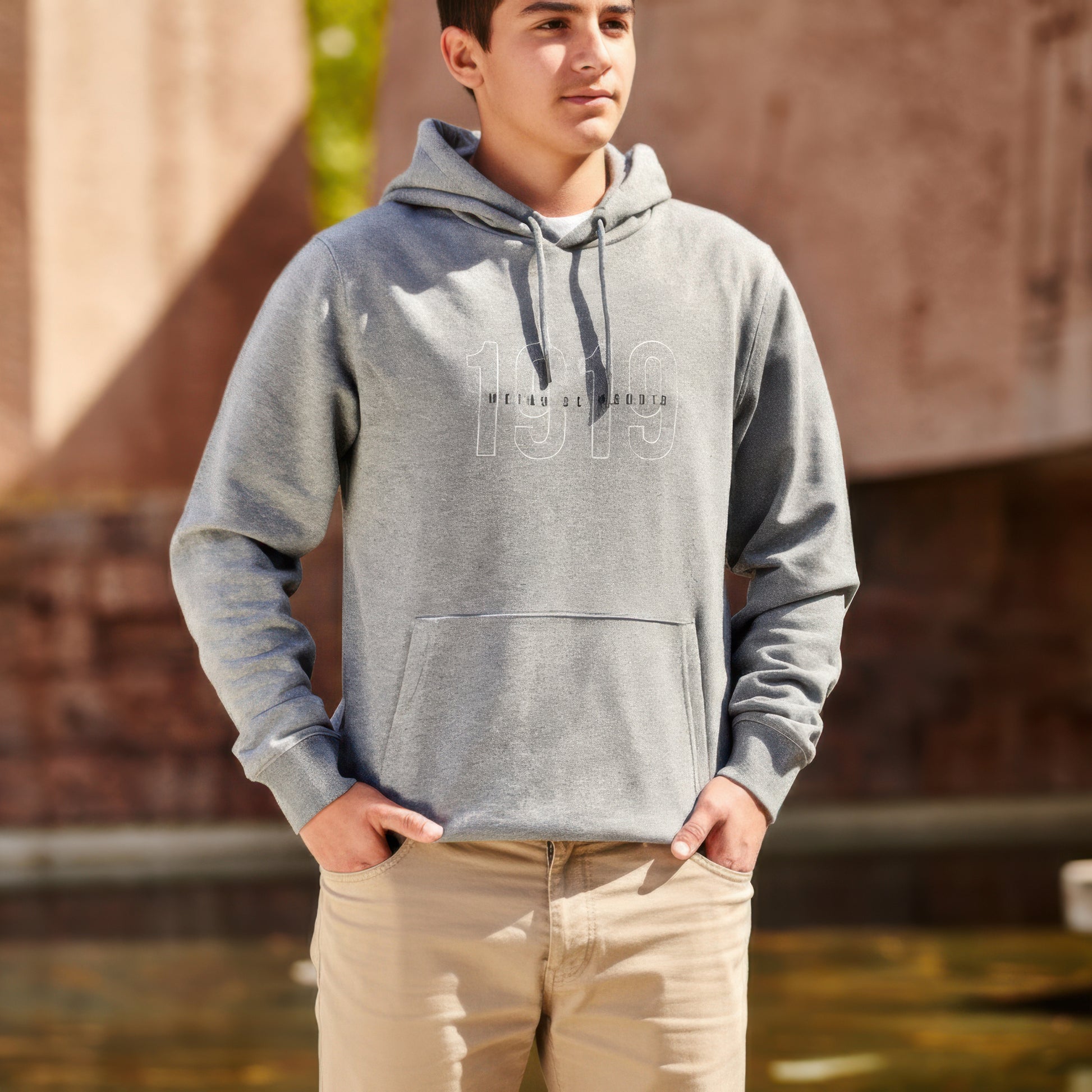 Joven con sudadera gris 1919 y pantalón beige de pie al aire libre