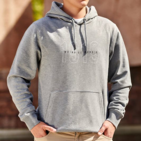 Joven con sudadera gris 1919 y pantalón beige de pie al aire libre